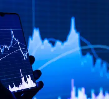 a person holding a cell phone in front of a stock chart