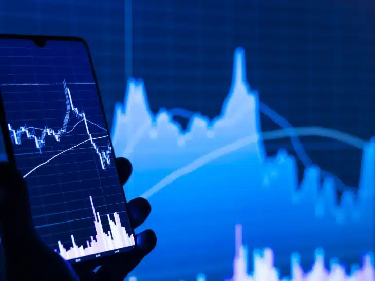 a person holding a cell phone in front of a stock chart